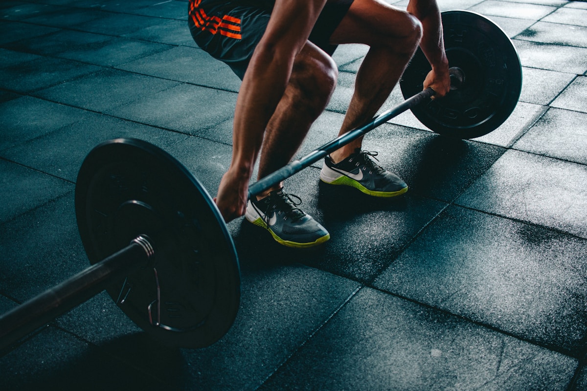 Athlete gripping a barbell on rubber gym flooring in a deadlift starting position